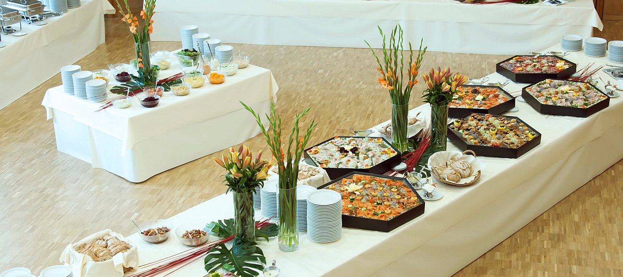 Angerichtetes Buffet auf weißer Tischdecke und Blumenschmuck